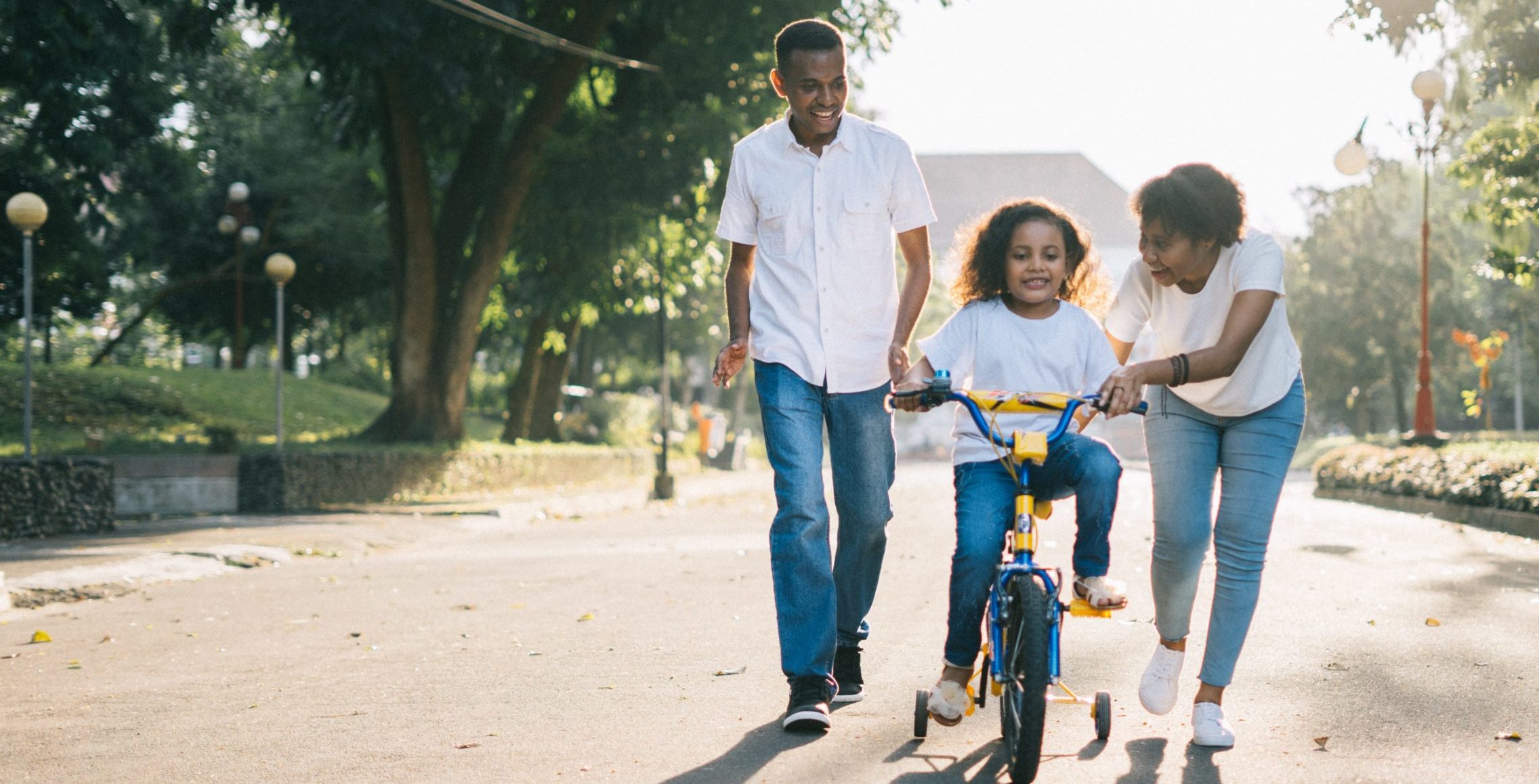 mom and dad teaching child to ride bike
