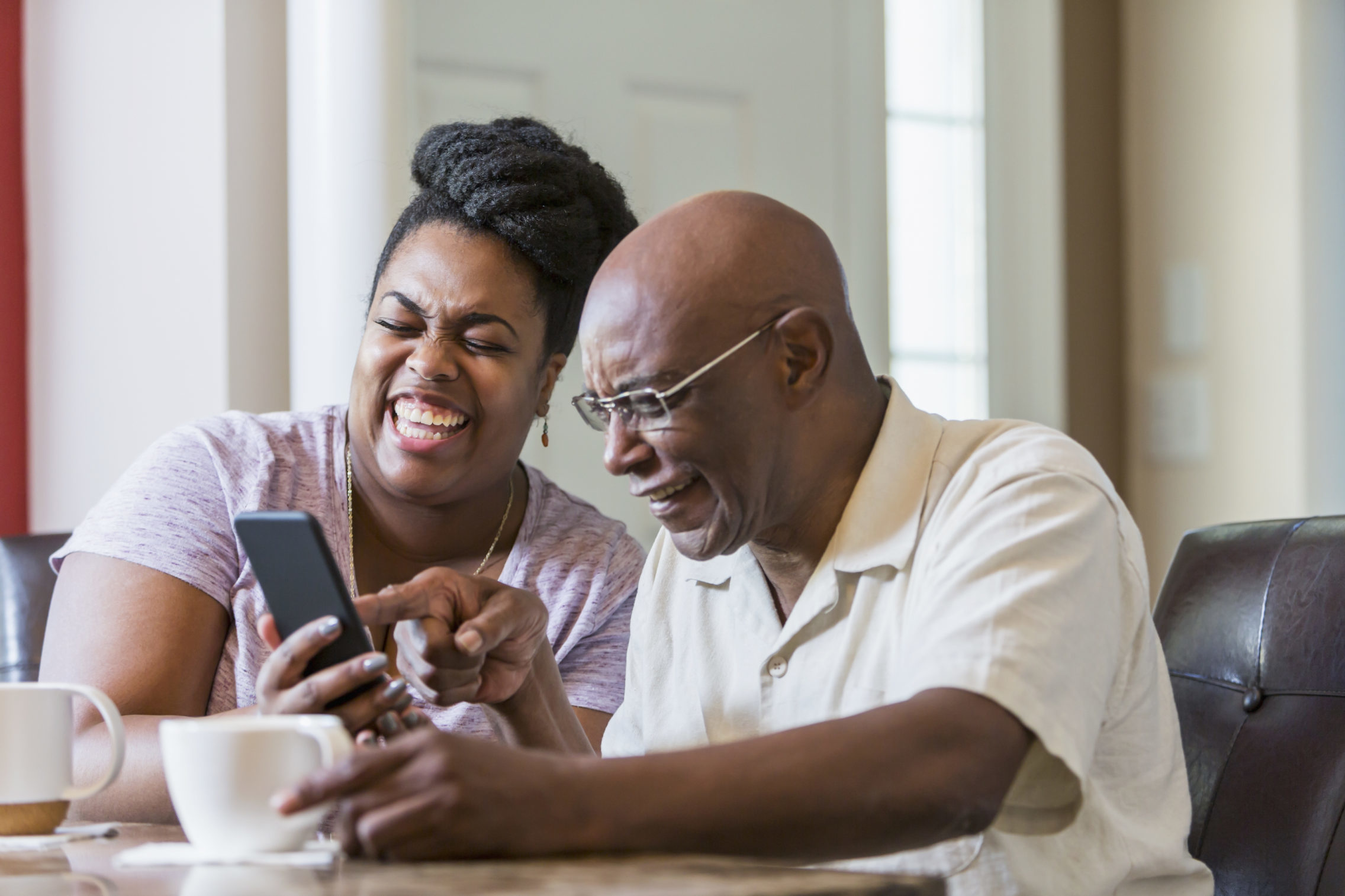 Senior man with adult daughter using smart phone laughing together