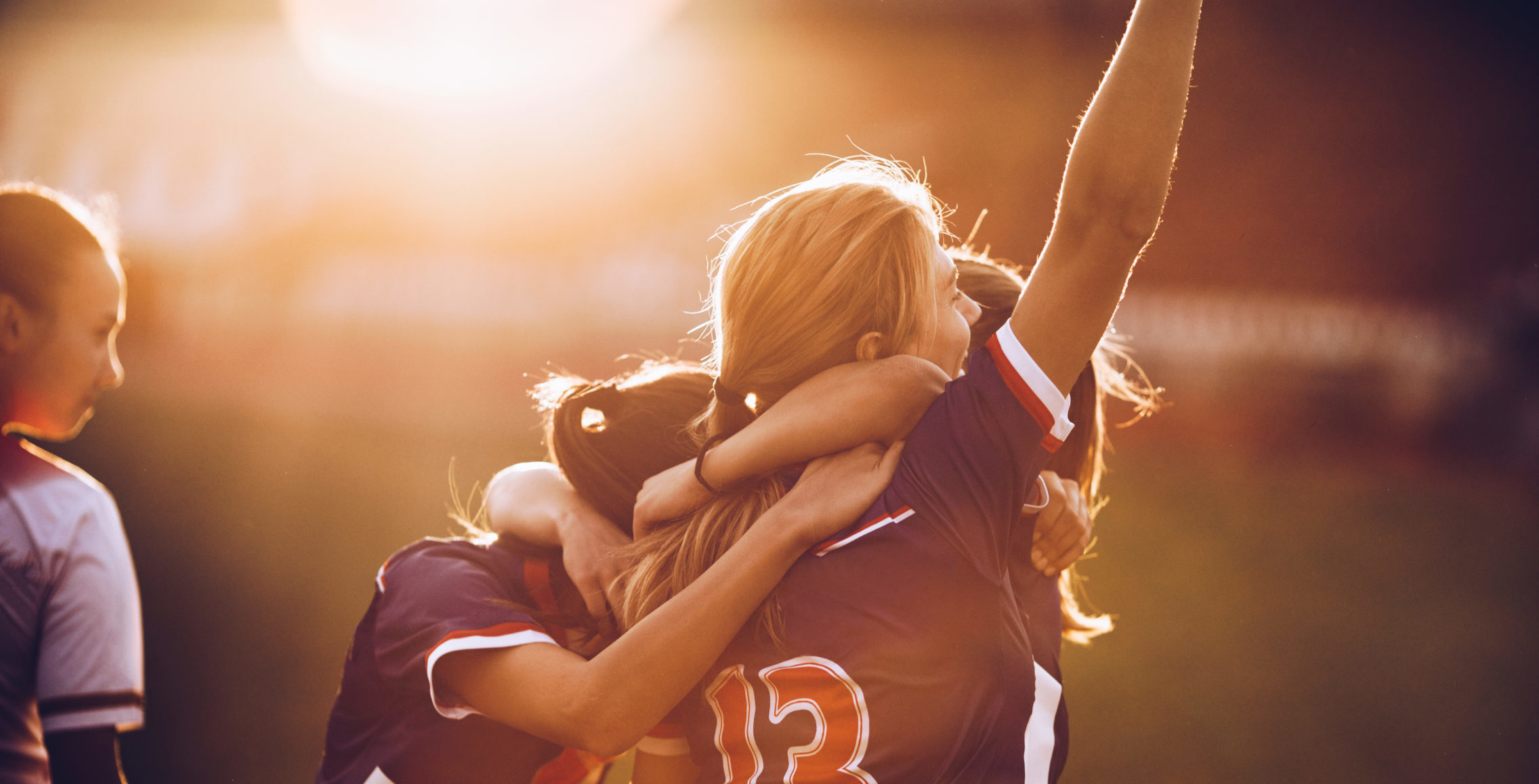 Three girls in jerseys celebrating the victory after soccer match