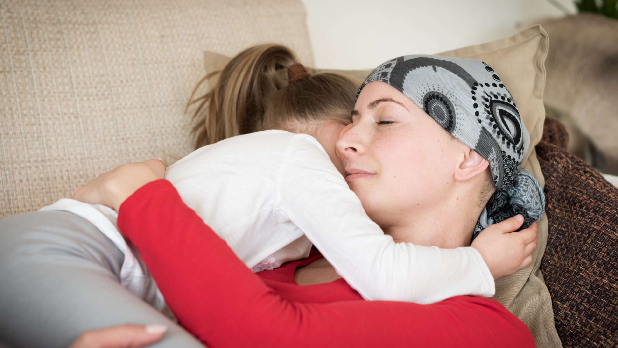 Young adult female cancer patient spending time with her daughter at home, relaxing on the couch.