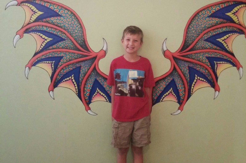 young boy posing in front of dragon wings painted on a wall