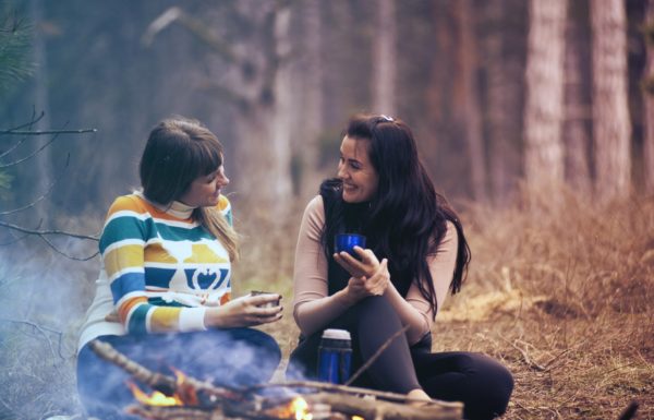 two women talking next to a campfire