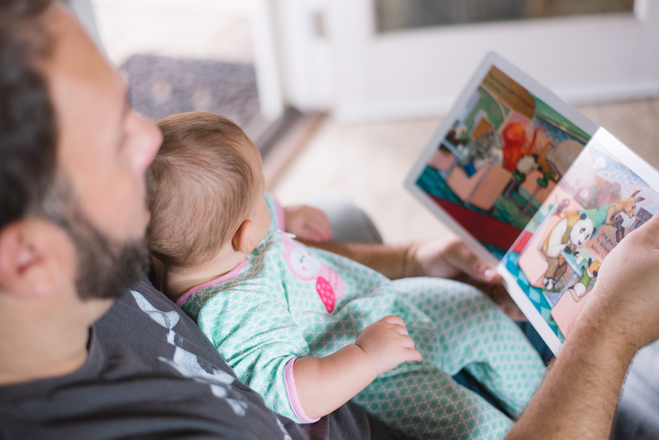father reading children's book to baby on chair