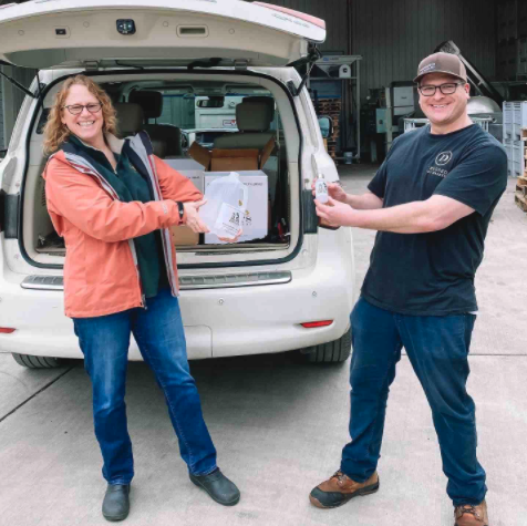 woman wearing orange jacket and man wearing black shirt holding up a box 