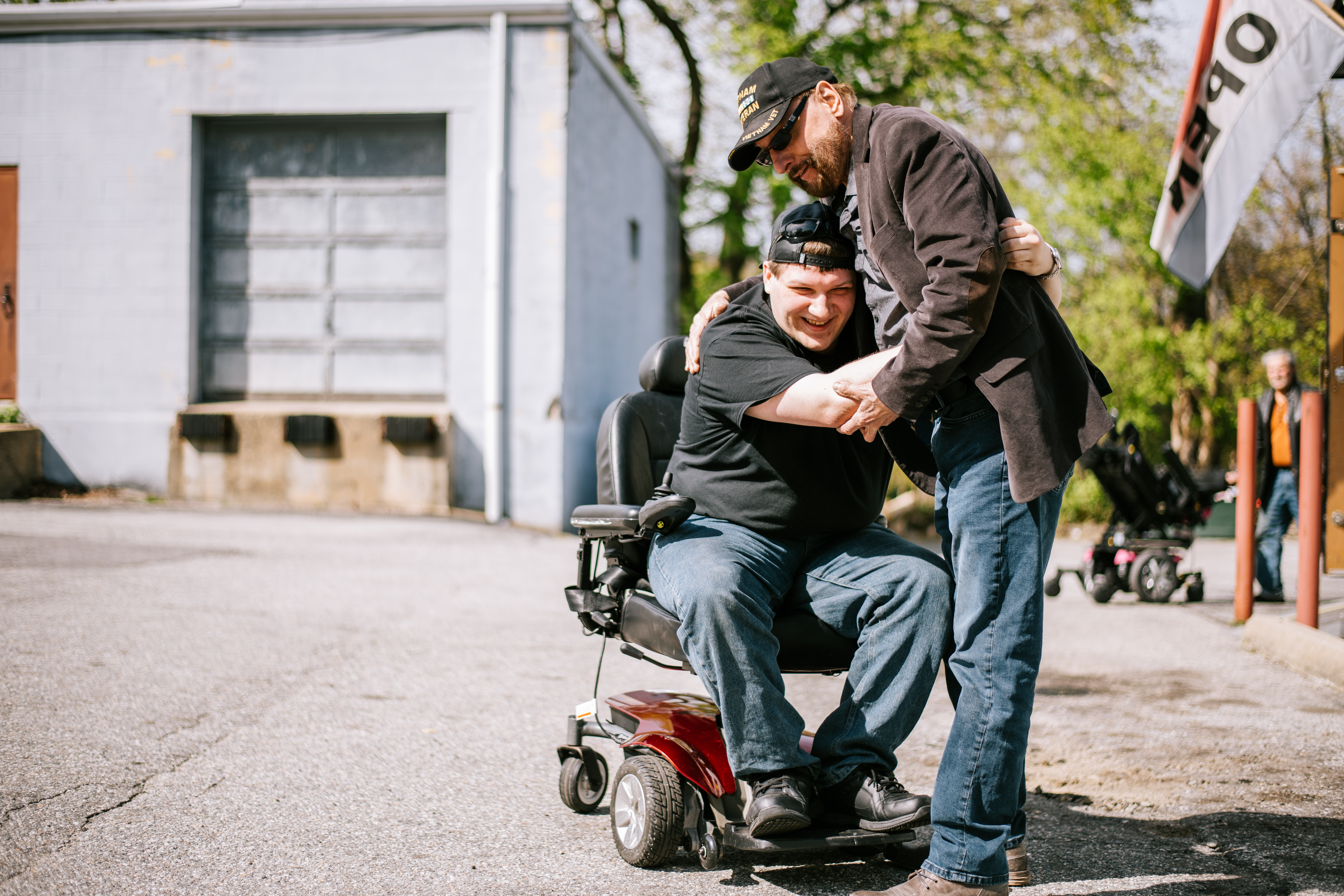 An older man hugs a man in a wheelchair