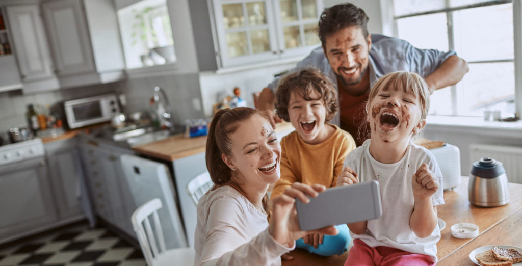 Couple avec ses enfants prenant un selfie dans la cuisine