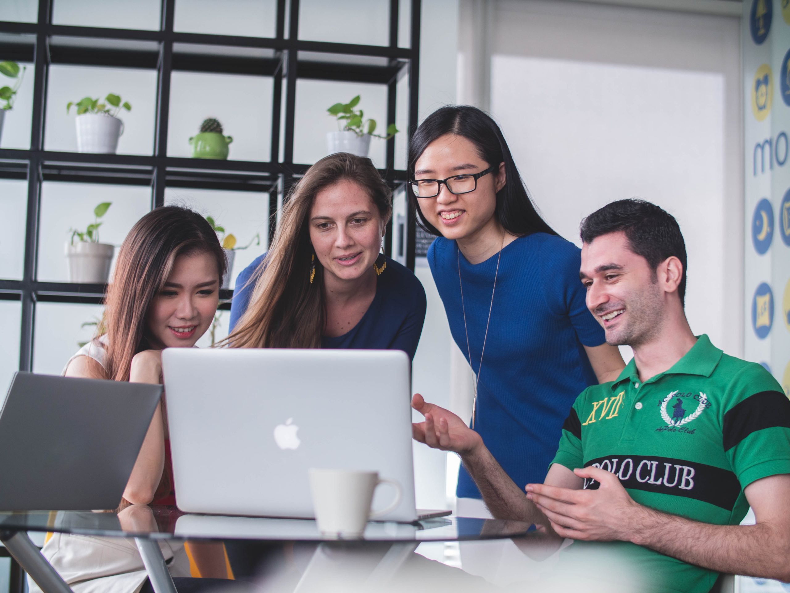 Four people in an office looking at a laptop screen and smiling